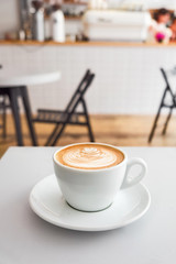 Flat white coffee with milk foam pattern on a white table with a coffee machine on a background. Vertical.