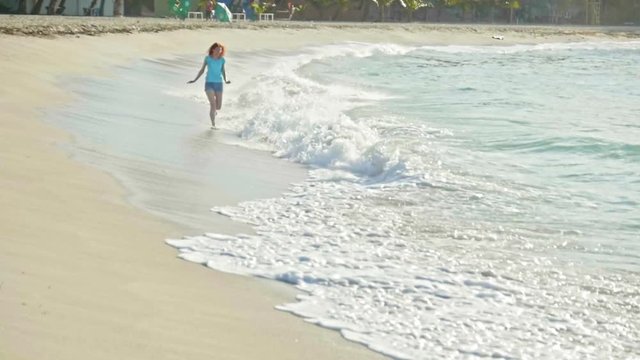 Young woman with long red hair in shorts pants play with waves running, feeling the sea, seascape, slow-motion, beach of Dominican Republic