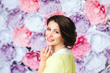 Beautiful young vintage woman in yellow dress smiling by the background of paper flowers. Beauty, fashion. Haircare. Cosmetics.