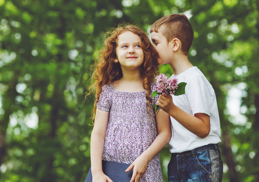 Little Boy And Girl Whispers In Spring Park.