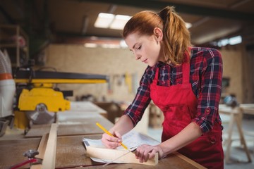 Female carpenter marking on wooden plank with pencil