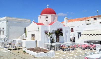 A white church with red roof and taverna tables on Mykonos island, Greece