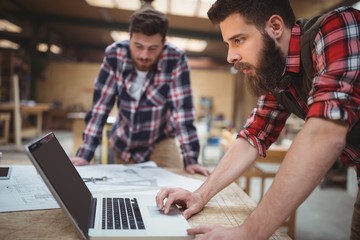 Carpenter using laptop while working on a blueprint