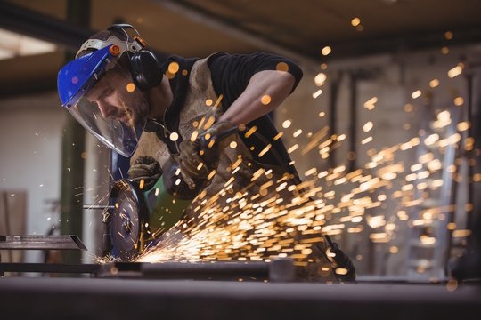 Welder cutting metal with grinder in workshop