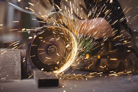 Close up of welder cutting metal with grinder in workshop