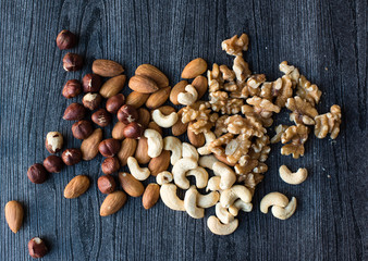 High angle view of hazelnuts, almonds, walnuts and cashews scattered on a black woodgrain background