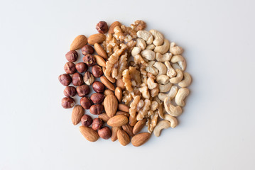 High angle view of hazelnuts, almonds, walnuts and cashews arranged in a circular shape on a white background