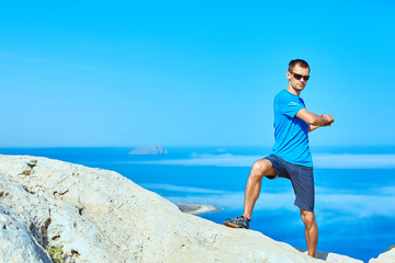 young man doing sports workout on the cliff against sea and blue sky at early morning
