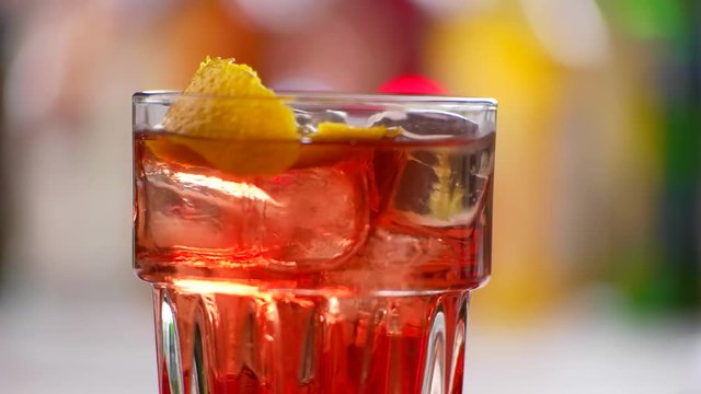 Glass with red cocktail rotates. Lemon peel inside a drink. Try the taste of nightlife. Cold and fresh negroni.