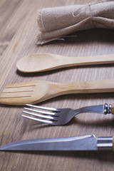 Cookware. Knife and fork with wooden handle, wooden spoon and fork, and napkin on brown wooden table