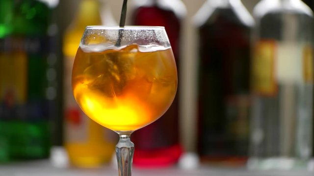 Spoon mixes orange beverage. Wineglass filled with drink. Chilled aperol spritz. Dry wine and soda water.