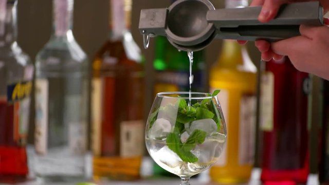 Lemon juice pours into beverage. Man's hands use lemon squeezer. Citrus juice for hugo cocktail. Work of bartender in club.