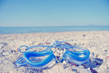 Blue swimming goggles on the white sandy beach, with sea in the background; ground level view. Filtered image in faded, retro, Instagram style. Nostalgic concept of exotic summer travel and holidays. - 113130066