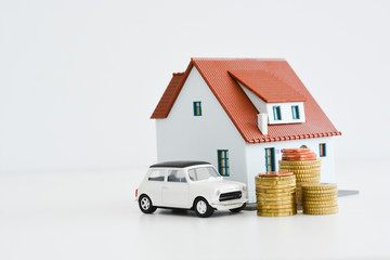 Car and house model with stack of coins isolated on white background