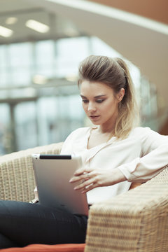 девушка с планшетным компьютером сидит в кресле и читает сообщение