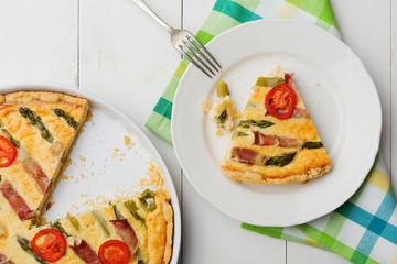 Tart with asparagus and tomatoes on white wooden background.