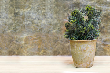 plastic tree in pot on wooden table and stone background, home d