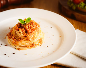 Close up of a plate of twirled spaghetti topped with delicious bolognaise sauce and basil