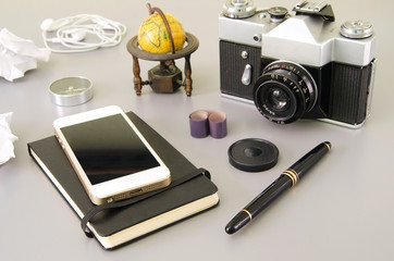 Travel essentials : vintage camera, black notepad, mobile, compass, pen on grey background. Concept for vacation o tourism.