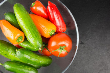 Washed organic vegetables in bowl on dark stone plate, top view