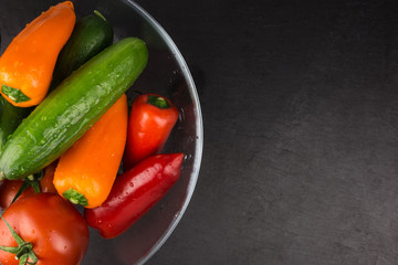 Washed organic vegetables in bowl on dark stone plate, top view