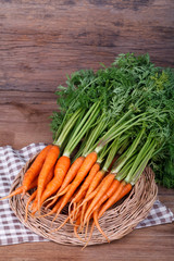 Bunch of fresh carrots with green leaves over wooden background