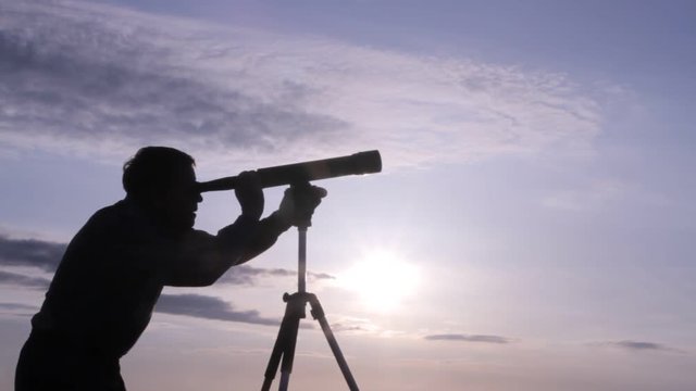silhouette of a man watching through a telescope