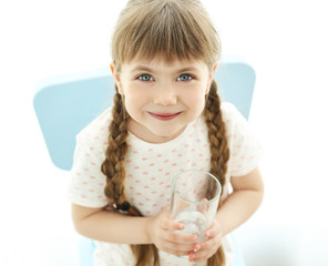 Cute little girl holding glass of water on light background