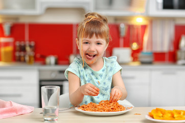 Adorable little girl eating spaghetti at table