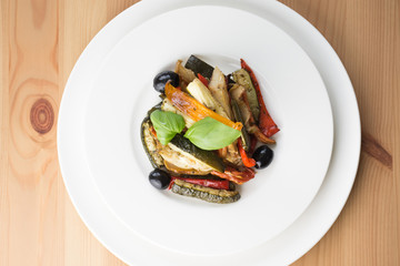 Roasted vegetables on a white plate on wooden background. Top vi