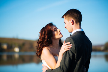 Beautiful happy young bride kissing handsome groom in sunlit park