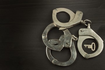 Metal police handcuffs on a dark wooden board. Silver handcuffs. Security concept on wooden background. Closed handcuffs. Equipment police officer. Crime and Punishment.
