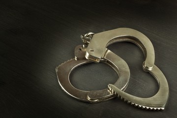 Metal police handcuffs on a dark wooden board. Silver handcuffs. Security concept on wooden background. Closed handcuffs. Equipment police officer. Crime and Punishment.
