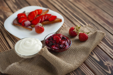 Toasts with cutted and fresh strawberry with sour cream and berry jam on wooden backcround