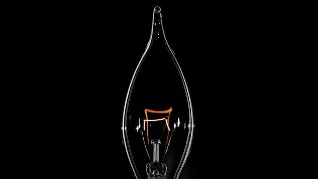 Candle shaped Edison lamp flickers over black background, macro view