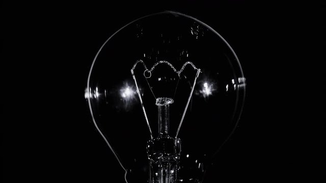 Tungsten light bulb lamp blinking over black background, macro view, loop ready