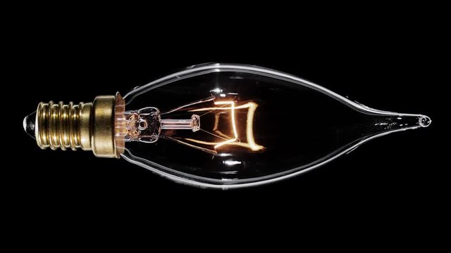 Candle shaped lamp light bulb flickers over black background, macro video, looped