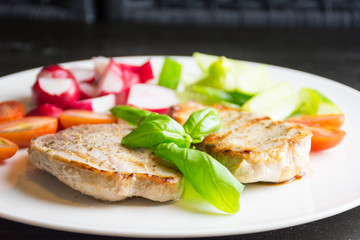Pork steaks with vegetables on white plate on dark background