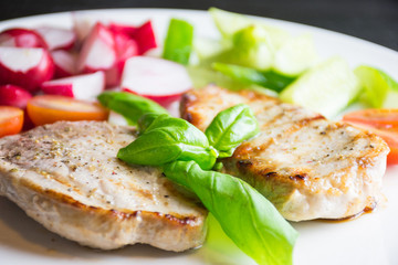 Pork steaks with vegetables on white plate on dark background