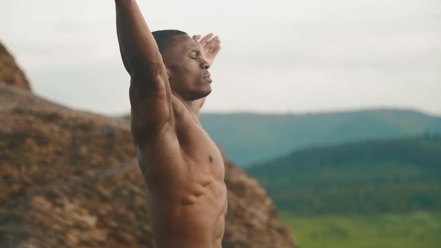 Close-up of handsome african american bodybuilder stretching outdoor. Mountain landscape background
