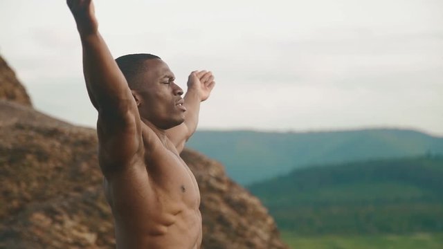 Side view of strong african american bodybuilder stretching outdoor. Mountain landscape background. Moment of harmony with nature