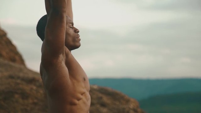 Side view of strong african american bodybuilder stretching outdoor. Mountain landscape background