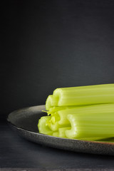 Dark food background with  celery on metallic dish,  front view.
