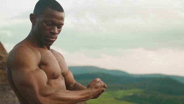 Close-up of muscular african american athletic man with naked torso showing his muscles. Green mountain nature background