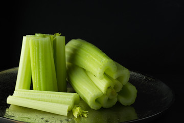 Dark food background with washed celery pieces on metallic dish,