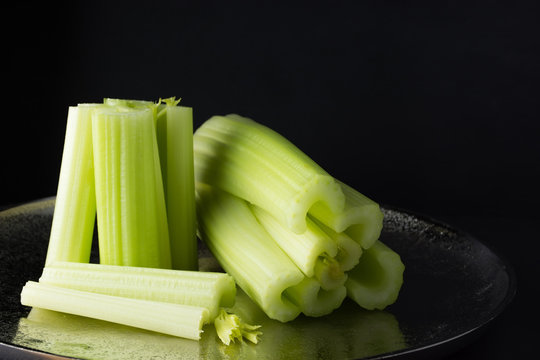 Dark food background with celery pieces on metallic dish, front