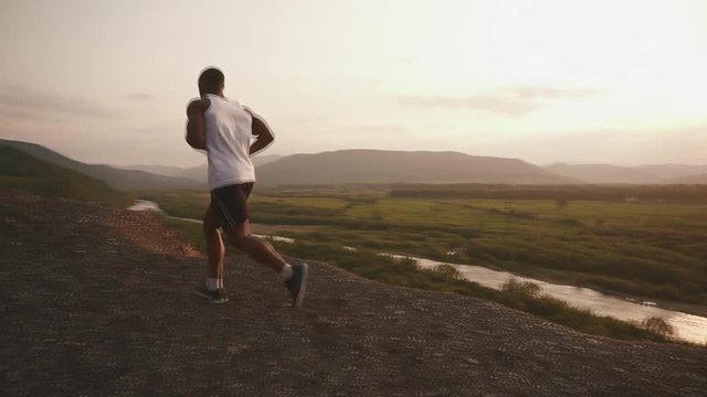 Strong african american muscular bodybuilder jogging outdoor. Rocky mountain landscape background