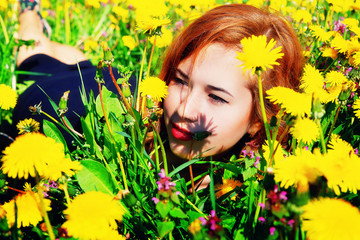 girl with red hair lying on the field of dandelions