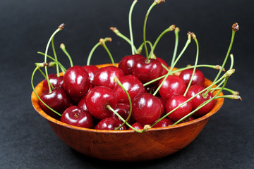 Ripe red cherries in a wooden bowl isolated on black background