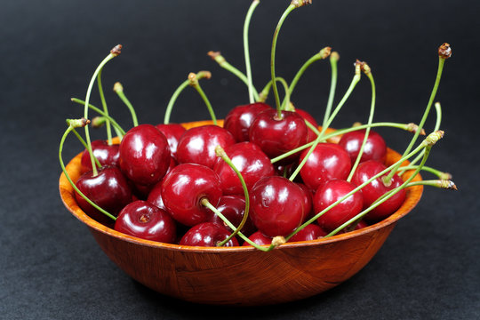 Ripe red cherries in a wooden bowl isolated on black background